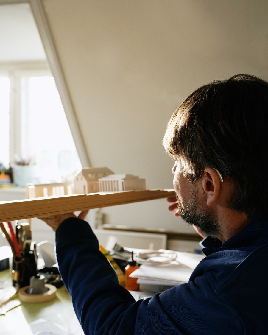 A designer holding a small wooden scale model up to the light to check its proportions